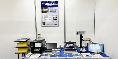 自動認識総合展名古屋の展示ブースにて、テーブルの上に金属対応RFIDタグとシンプルなスマートカメラ「SimPrun」と新開発！プリンタブル金属対応RFIDタグが置かれている様子。
